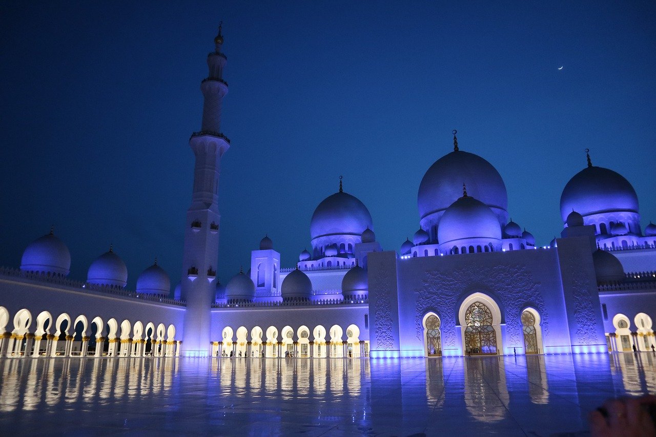 A bunch of vegetables on display lit up at night with Sheikh Zayed Mosque in the background